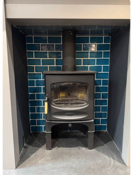 Modern wood burner installed in a blue-tiled chimney recess